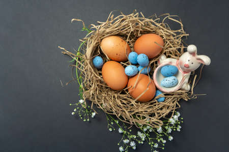 Natural eggs with Easter eggs, feathers in a nest on a dark background. Top view, Happy Easter....