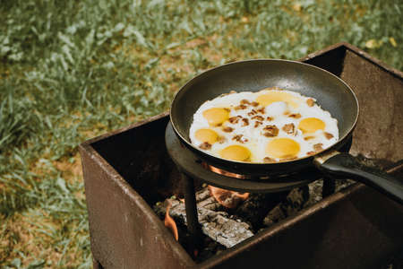 Frying pan of fried eggs and bacon, green grass on the background, cooked on the grill on a summer sunny day, summer breakfast, eating in nature - the concept of a healthy lifestyleの写真素材
