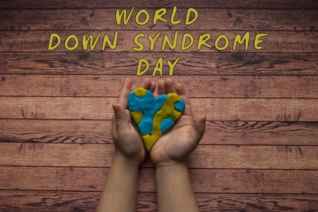 Child's hands holding a yellow and blue heart on dark wooden background with text.の写真素材