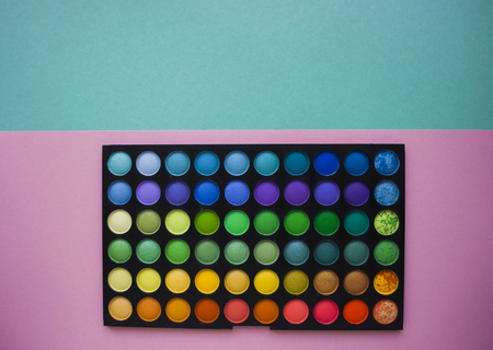 Pallet of different color eyeshadows on bright colorful background with space for your text.