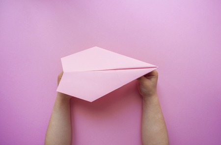 Child's hands holding pink paper plane on pink color background with space for your text.の写真素材