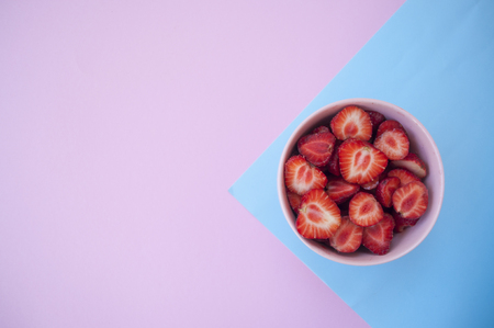 A pink bowl full of beautiful fresh juicy strawberries on pastel pink and blue background with text space.の写真素材