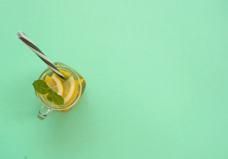 Top view of mason jar glass of lemonade or mojito with lemons and mint on turquoise background with...