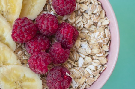 Close up of oatmeal in a beautiful pink bowl with fresh sweet rasberry and banana slices on...