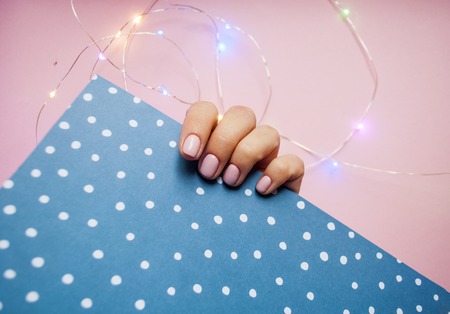 Young woman's hand with beautiful manicure on pink and blue background with light garland. Minimal style backgroundの写真素材