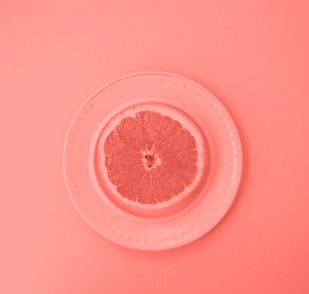 Ripe juicy cut grapefruit on a plate on coral background. Color of 2019.の写真素材