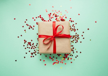 Gift box tied with red ribbon on pastel pink background.