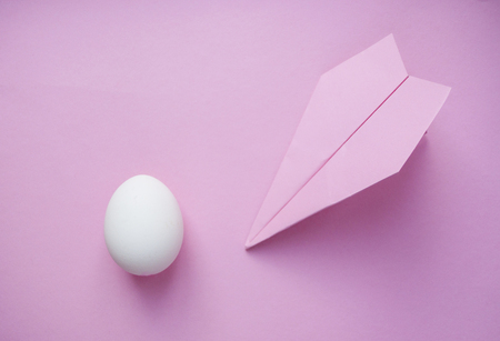 A white single egg on pink background with paper plane and copyspace. Travel concept.の写真素材