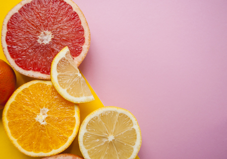 Flat lay of cut ripe juicy grapefruit, lemon and orange on pink and yellow background with copyspace.の写真素材