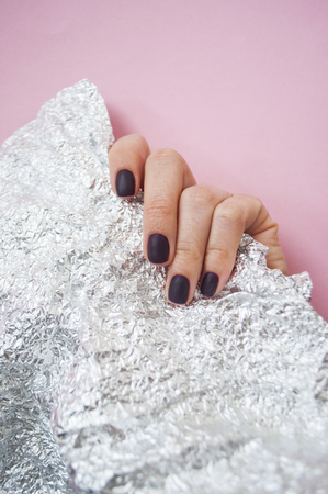 Young woman's hand with beautiful manicure on pink background holding metallic shiny paper.の写真素材