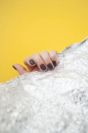 Young womans hand with beautiful manicure on yellow background with metallic shiny paper.の写真素材