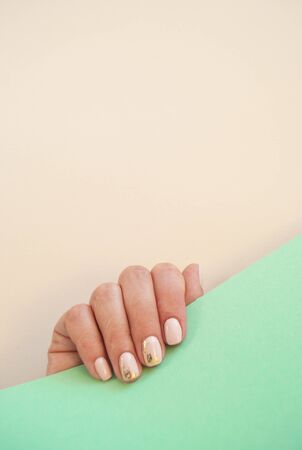 Young woman's hand with beautiful manicure on beige and turquoise background with copyspace. Vertical picture.の写真素材