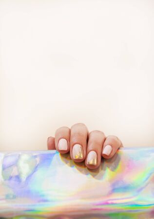Young woman's hand with beautiful manicure on beige background holding metallic holographic paper.の写真素材