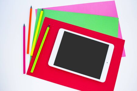 Colorful paper, neon pencils and tablet on white background with copyspace. Flat lay style. Back to...