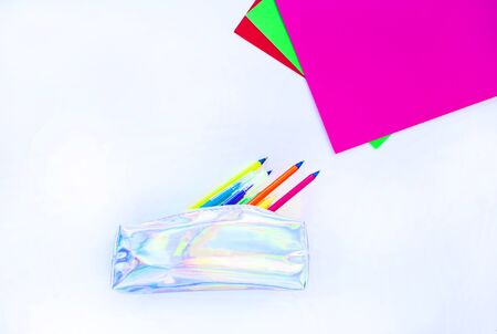 Colorful paper, neon pencils and holographic pencil case on beige background with copyspace. Flat...