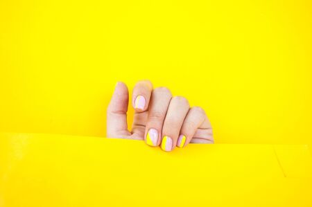 Young woman's hand with beautiful manicure on yellow color background holding bright yellow paper.の写真素材