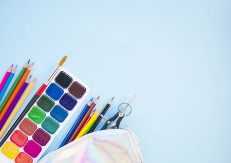 Colorful pencils, watercolors, holographic pencil box on blue background with copyspace. Flat lay style. Back to school concept.の写真素材