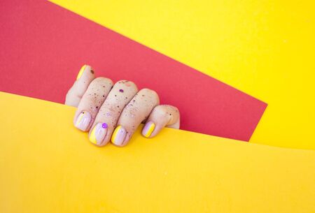 Young womans hand with beautiful manicure on yellow and red background holding yellow color paper with copyspace.の写真素材