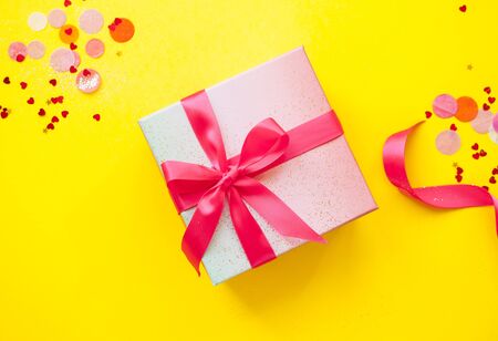 Giftbox tied with pink color ribbon on bright yellow background with sparklets and confetti. Flat lay style.の写真素材