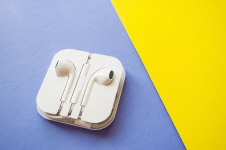 Earphones in a white plastic case on a bright yellow and blue background.の写真素材