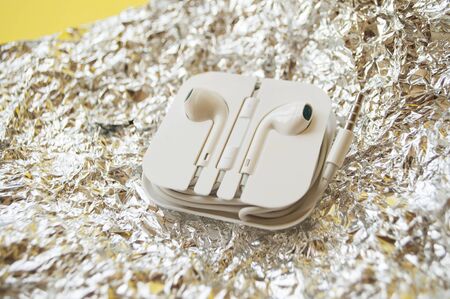 Earphones in a white plastic case on a bright yellow and shiny metallic background.