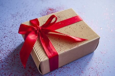 Close up of giftbox tied with bright red color ribbon on purple background with sparklets and...