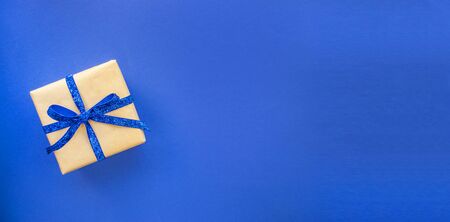 Flat lay of giftbox tied with classic blue color ribbon on blue background. 2020 color trend. Banner with place for text.の写真素材