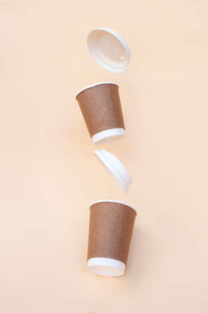 Brown sustainable paper coffee cups on a beige background with one of the cups flying. Zero waste...