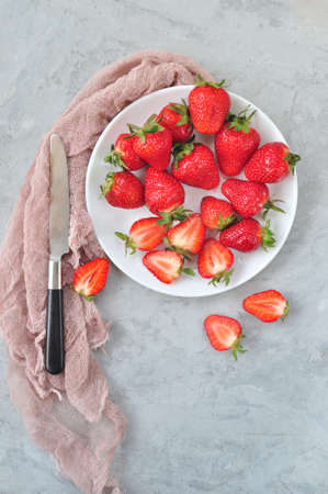 Flat lay of fresh ripe sweet strawberries on a white palte with a knife and kitchen textile on a gray color background.の写真素材
