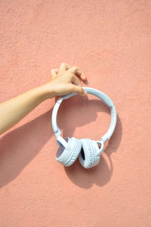 A girl hand holding modern wireless headphones on a pink background.の写真素材