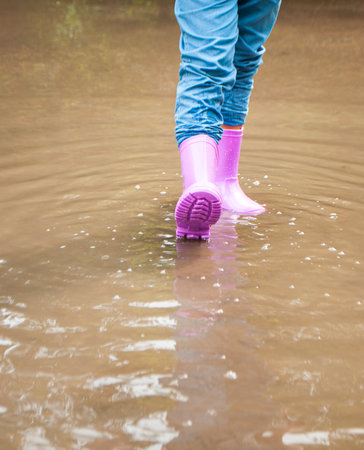 A girl in purple rubber boots is playing in muddy puddles.の写真素材