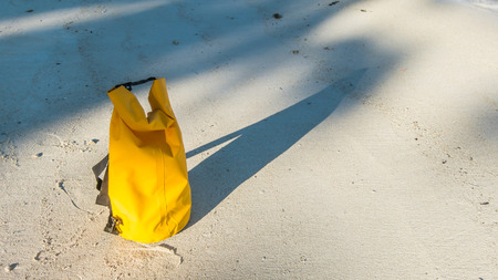 Light and shadow on sandy beach with yellow waterproof bag