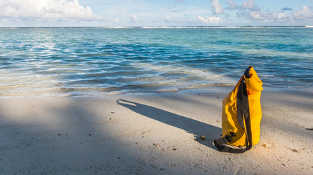 Light and shadow on sandy beach with yellow waterproof bagの写真素材