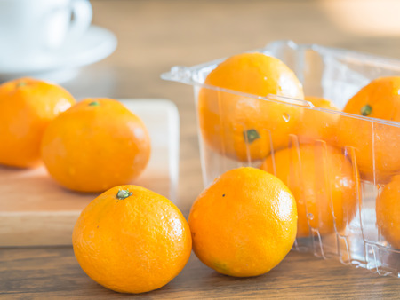 Oranges, wooding cutting board on the table in the kitchen with blurry white coffee cup background. Dieting or healthy concepts.の写真素材