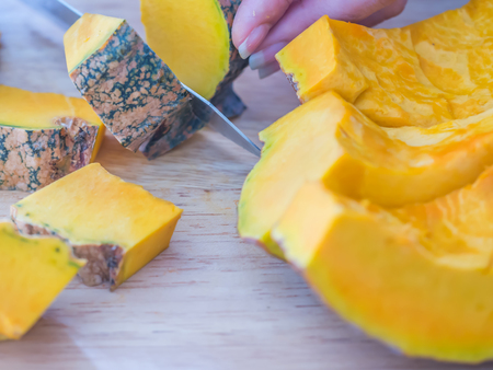 Pumpkin preparation and cooking concepts. Woman cut pumpkin into small pieces by knife on wooden cutting board.の写真素材