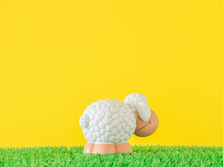White sheep toy standing beside on artificial grass
and yellow cement backgroundの写真素材
