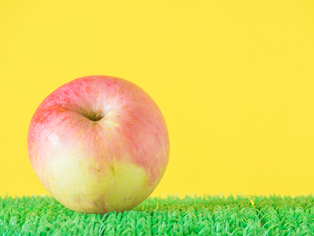 Apple on artificial green grass and yellow backgroundの写真素材