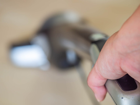 Closeup of woman 's hand with blurry vacuum cleaner and wooden floor.の写真素材
