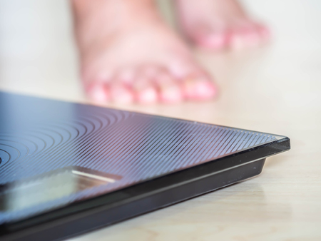 Closeup of body weight scale with blurry woman 's feet on wooden floor.の写真素材