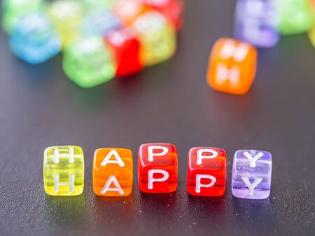 Selective focus at happy word with many blurry multicolored and colorful of alphabet plastic box on black board background. Happiness concepts and ideas.の写真素材