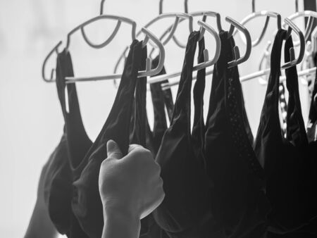 Black and white tone of woman 's hand and stack of clothes hanger with black sports bras after laundry or washing process.の写真素材