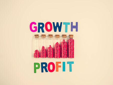 Cross processed tone effect. Multicolored wooden alphabet of profit growth text on light yellow pastel color background with small glass bottles, vivid or vibrant red gravel. Business growth concepts.の写真素材