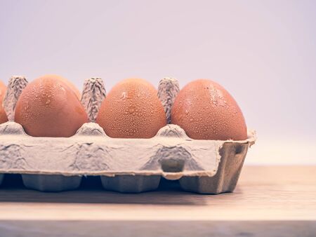 Closeup and cross processed tone of chicken brown eggs in paper carton tray on wooden cutting board...