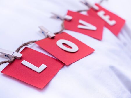 Wooden alphabets of love word and tweezers. Red note paper and hemp rope on white wrinkle cotton fabric texture background for love, romance, valentine 's day, wedding, honeymoon concept and idea. の写真素材