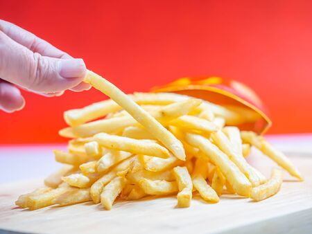 Closeup of french fried on wooden plate and woman 's hand with blurry red background.の写真素材
