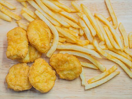 Top view or directly above of closeup crispy nuggets and french fried on wooden table.