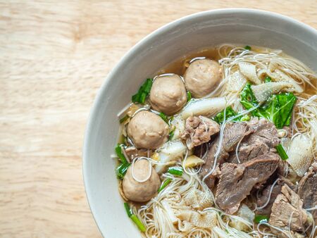 Top view or directly above of Thai braised beef noodle soup in ceramic bowl on blurry wooden table...