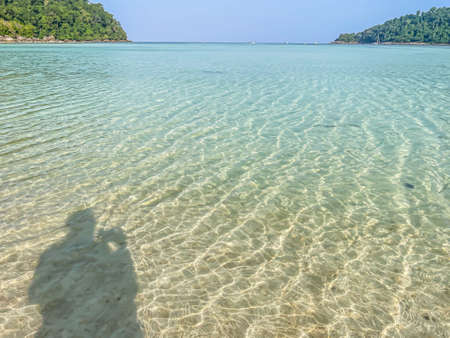 Blurry shadow of woman tourist take a landscape photo by mobile phone on   sea background with blurry island and blue sky for summer and travel concepts.の写真素材