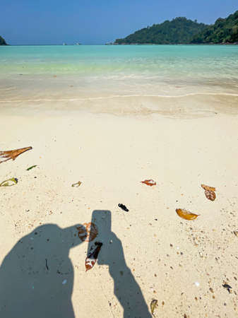 Shadow of woman photography with mobile phone on sand texture with beach, sea, island and blue sky for summer and travel concepts.の写真素材