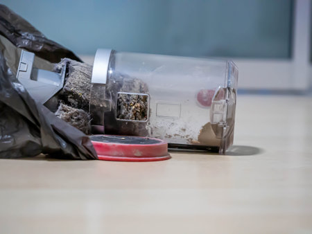 Closeup of a plastic vacuum cleaner garbage bin with black garbage bag and dust or rubbish on a wooden floor for cleaning conceptの写真素材